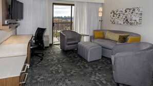 A hotel room with a desk, chair, sofa, ottoman, and a TV.