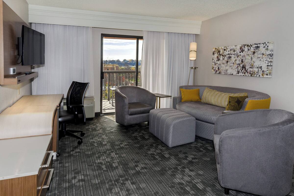 Una habitación de hotel con escritorio, silla, sofá, reposapiés y televisor.