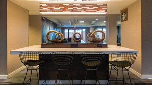 A modern bar area with a central island, three wire mesh chairs, and a decorative wall with circular patterns.