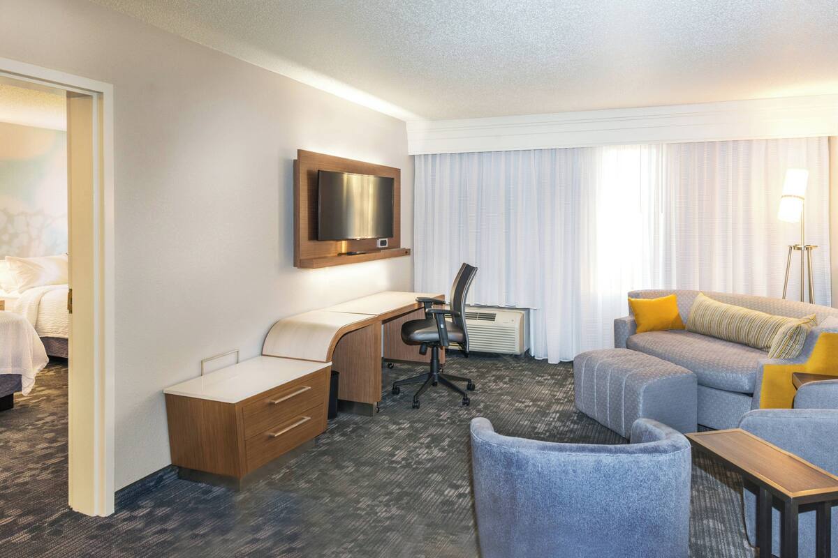Una habitación de hotel con una cama, un escritorio, una silla, un sofá y un televisor en la pared.