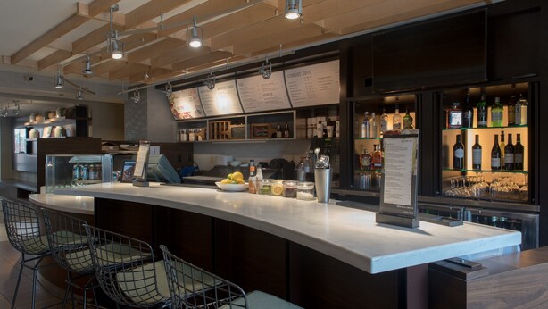 A modern bar area with a curved counter, bar stools, and a menu board.