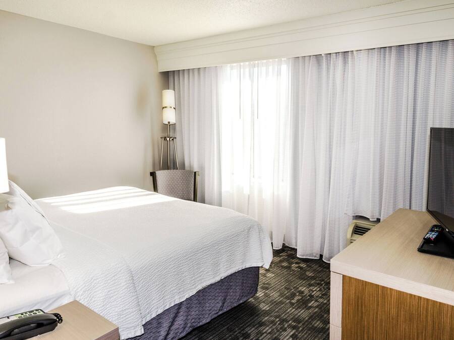 Ett hotellrum med en säng, ett skrivbord med en telefon, en lampa och en tv.