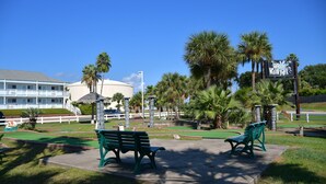 A park with two green benches, palm trees, and a sign for "Brevard Waterpark". - Inn at The Waterpark (Galveston)