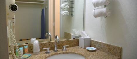 Un baño con lavamanos de granito, un espejo, toallero y artículos de aseo.