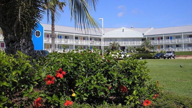 A hotel with a white exterior, multiple balconies, and a parking area with cars. - Inn at The Waterpark (Galveston)