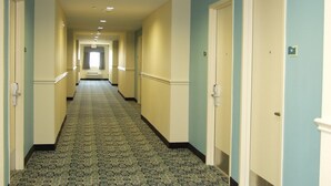 A hotel hallway with patterned carpet, cream walls, and white doors. - Inn at The Waterpark (Galveston)