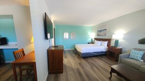 A hotel room with a bed, a desk, a chair, a sofa, and a TV. - Inn at The Waterpark (Galveston)