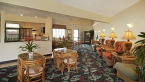 A hotel lobby with a dining area, seating arrangements, and a refrigerator. - Inn at The Waterpark (Galveston)