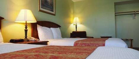 Camera d'albergo con due letti, ognuno con copripiumino rosso e bianco, due abat-jour, un comodino con il telefono e un quadro appeso al muro.