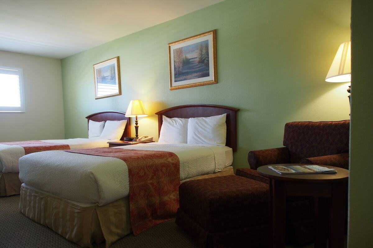 A hotel room with two beds, a chair, a small table, and a lamp.