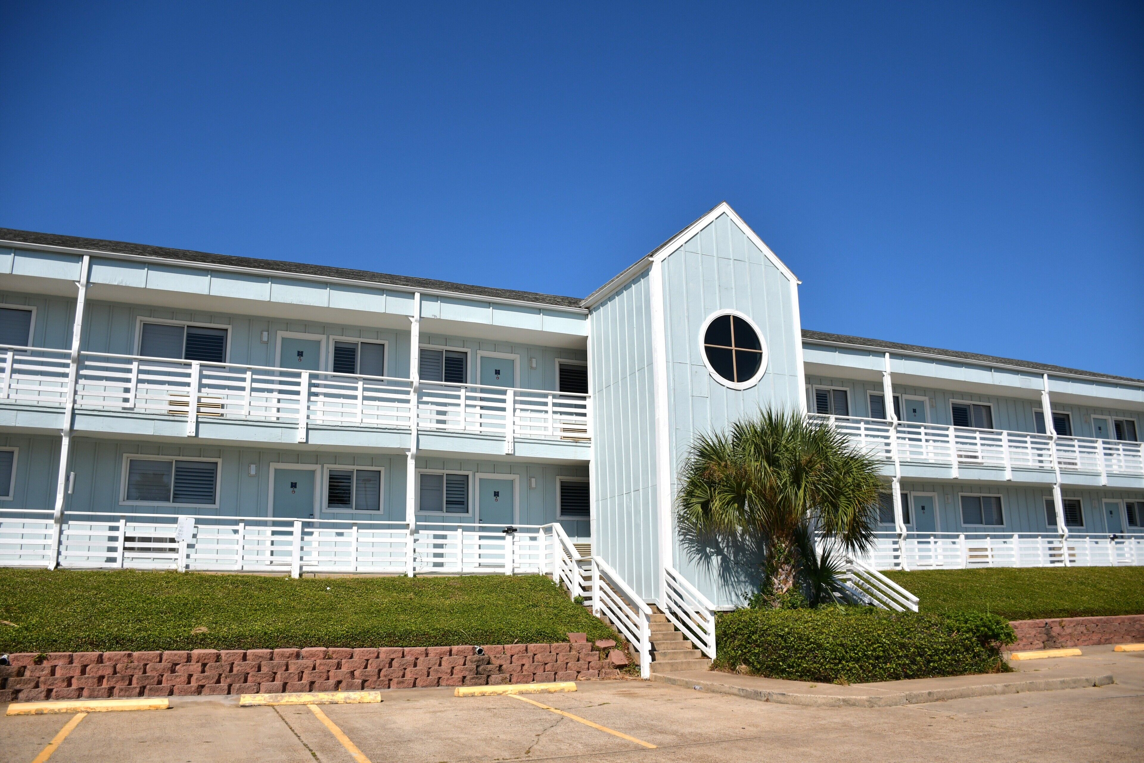A multi-story motel with a central tower, a parking lot, and a well-maintained lawn.