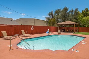 Relax by the clear pool surrounded by a brick border, lounge chairs, and a shaded pergola.