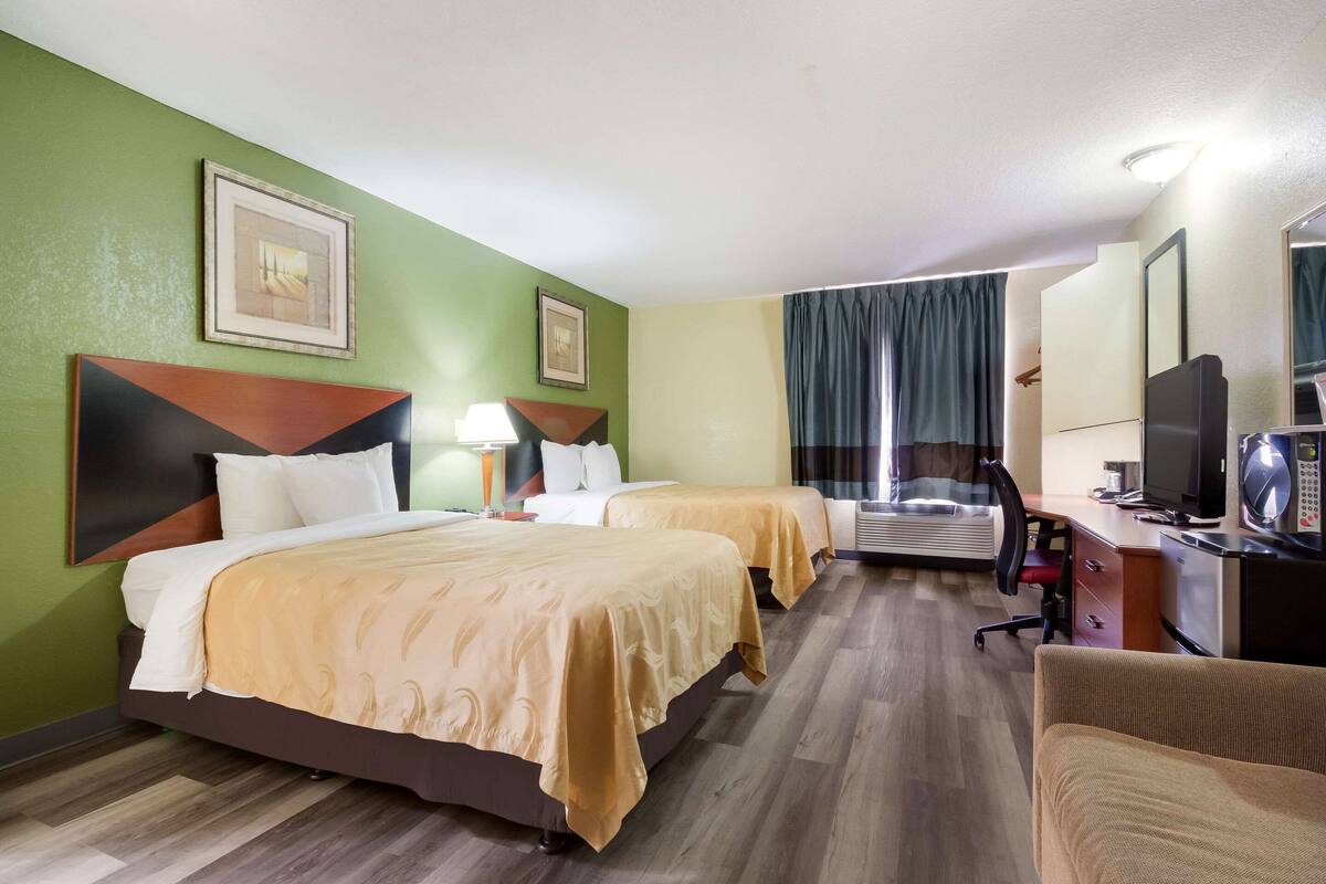 A hotel room with two beds, a desk, a chair, a TV, and a mirror.