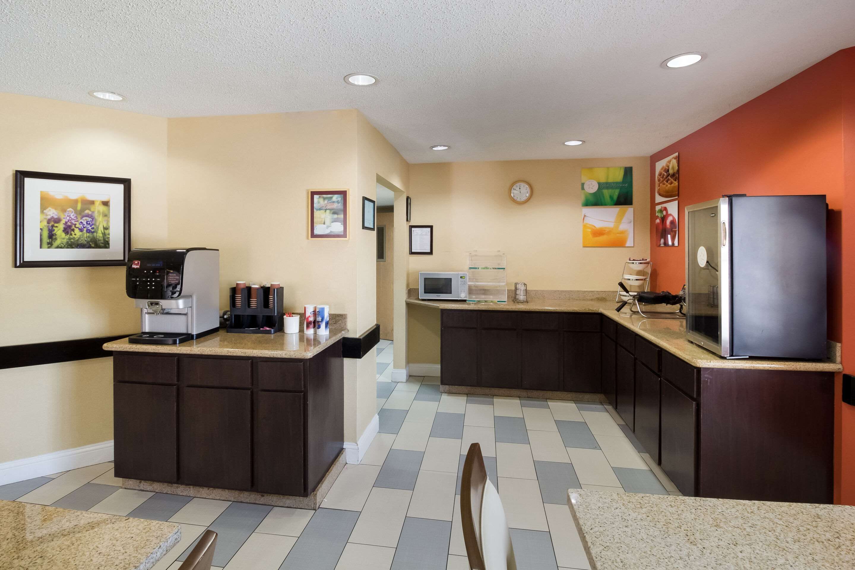 A compact kitchen with a coffee machine, microwave, refrigerator, and a clock on the wall.