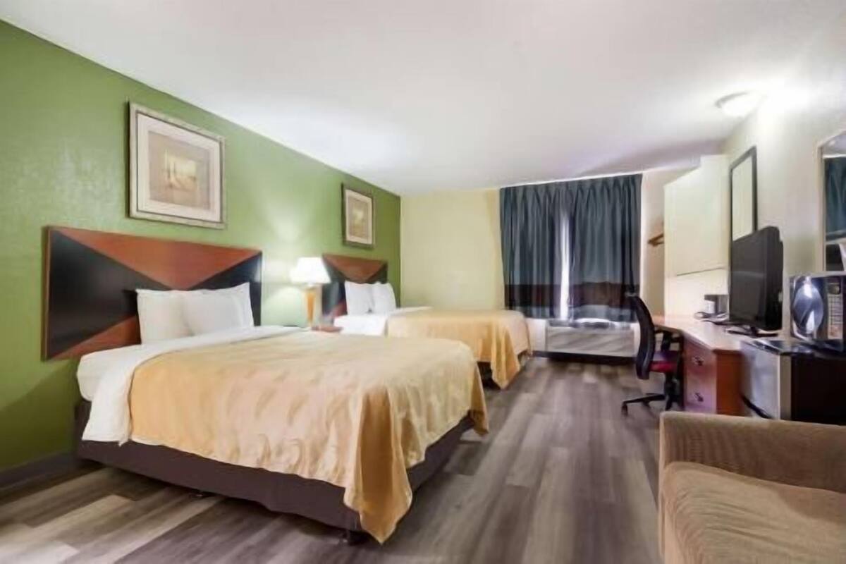 A hotel room with two beds, a desk with a chair, a television, and a window with curtains.