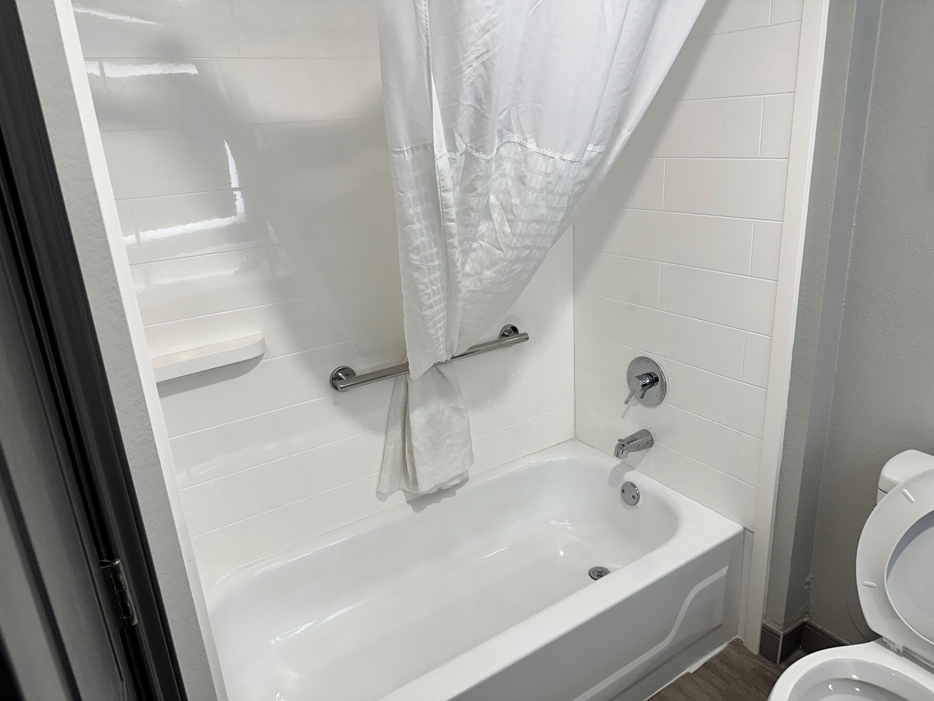A bathroom with a white bathtub, a shower curtain, a grab bar, and a toilet.