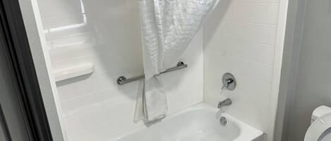 A bathroom with a white bathtub, a shower curtain, a grab bar, and a toilet.