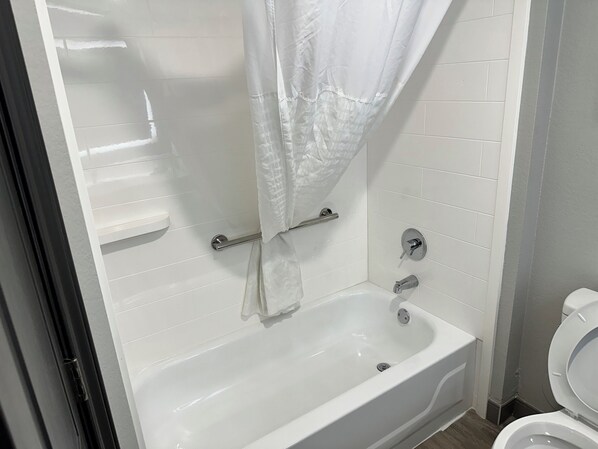 Un baño con una bañera blanca, cortina de ducha, barra de apoyo y un inodoro.