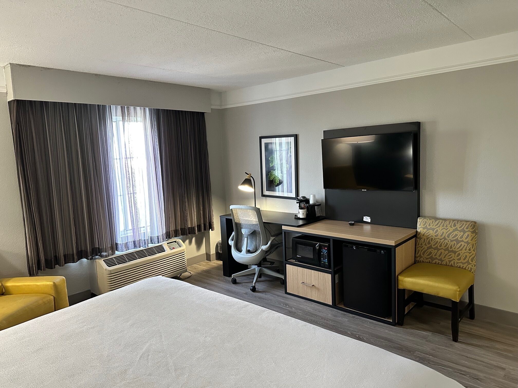 A hotel room with a large bed, a desk with a computer, a TV, and a chair.