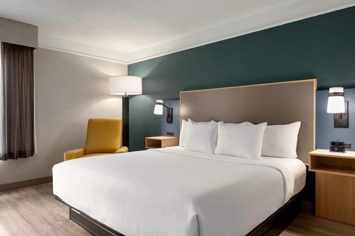 Ein Hotelzimmer mit einem großen Bett, einem Sessel, Nachttischen und Lampen.