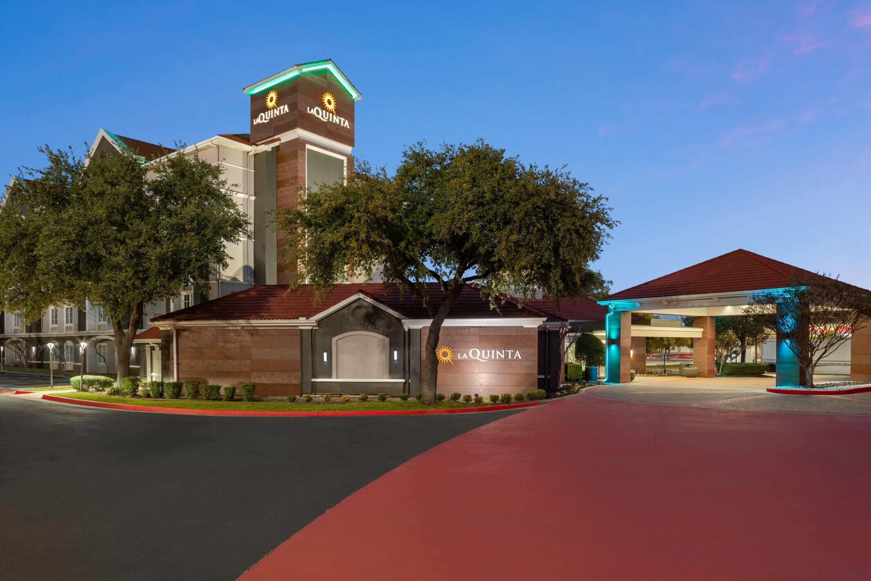 A hotel entrance with a prominent sign, a covered parking area, and a well-maintained lawn.