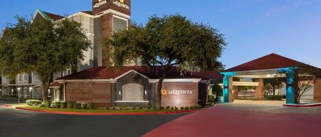 A hotel entrance with a prominent sign, a covered parking area, and a well-maintained lawn.