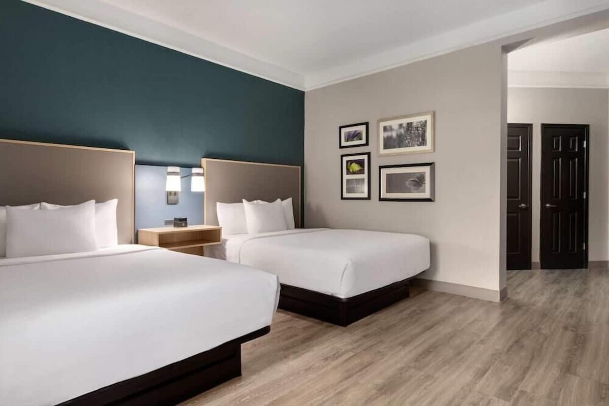 Ein Hotelzimmer mit zwei Betten, einem Nachttisch, einer Lampe und gerahmten Bildern an der Wand.