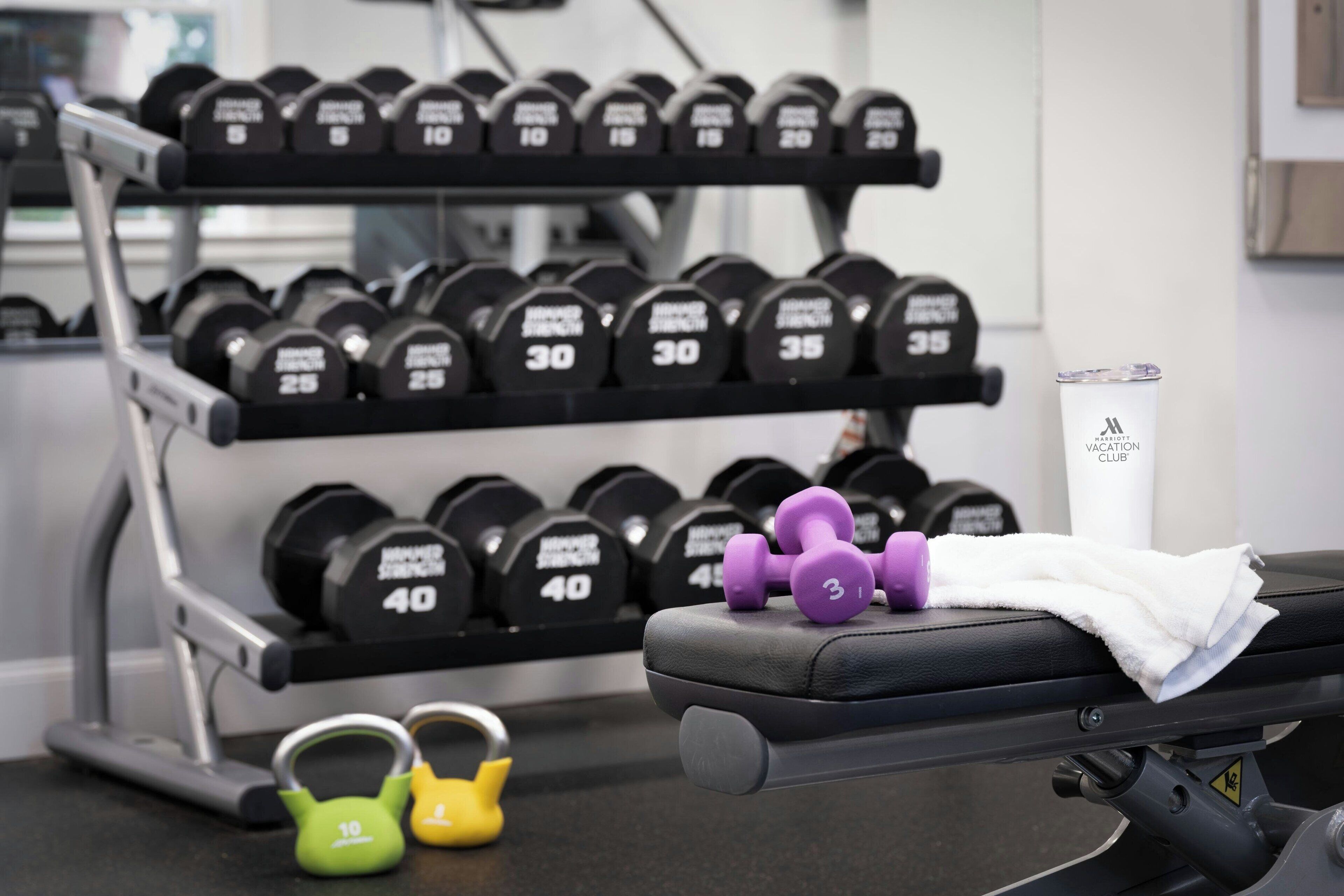 Et fitnessrum med bænk, kettlebells og vægtstangsstativ.