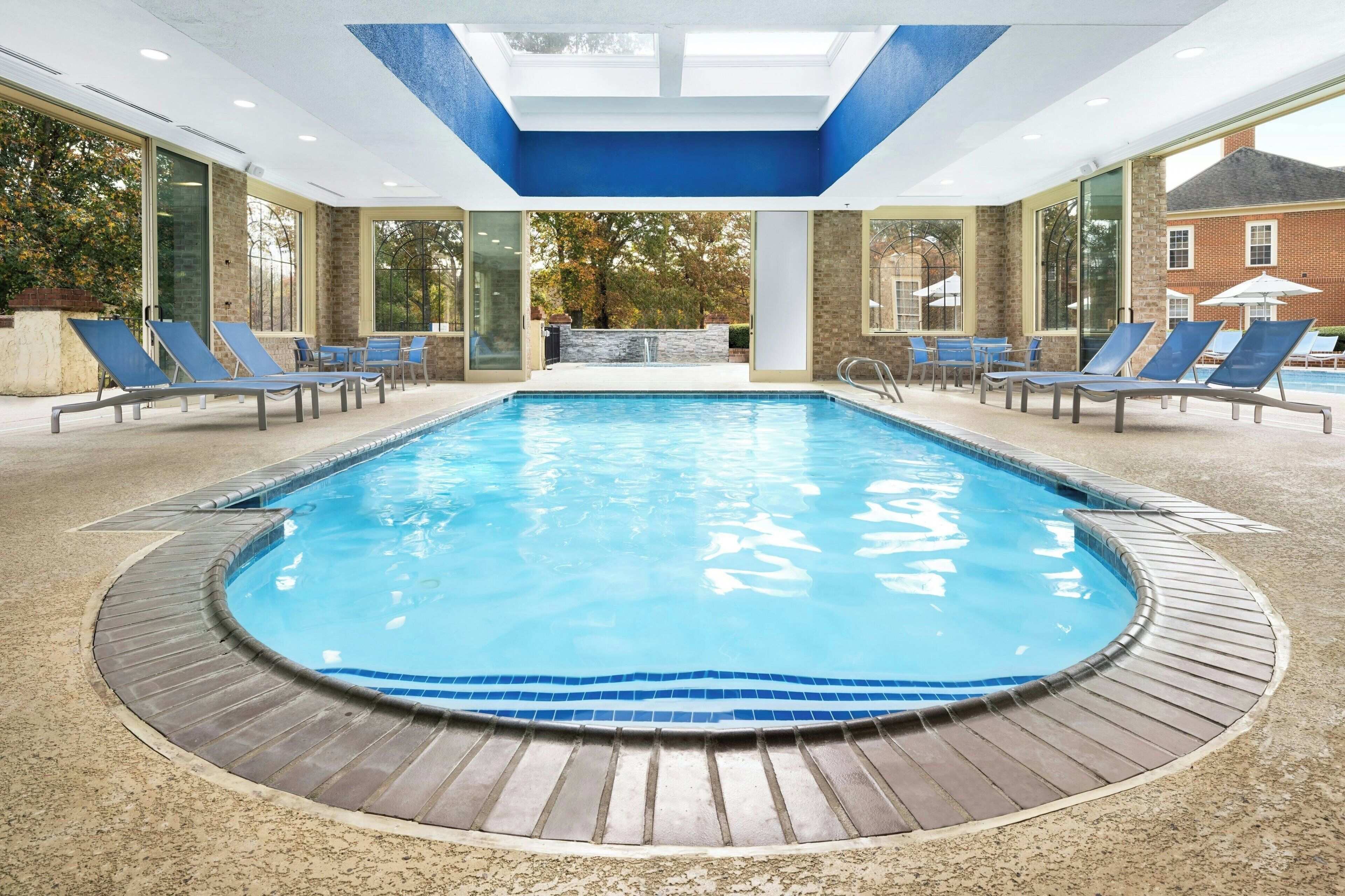 An indoor swimming pool with a tiled edge, surrounded by lounge chairs and a wooden deck.