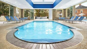 An indoor swimming pool with a tiled edge, surrounded by lounge chairs and a wooden deck.