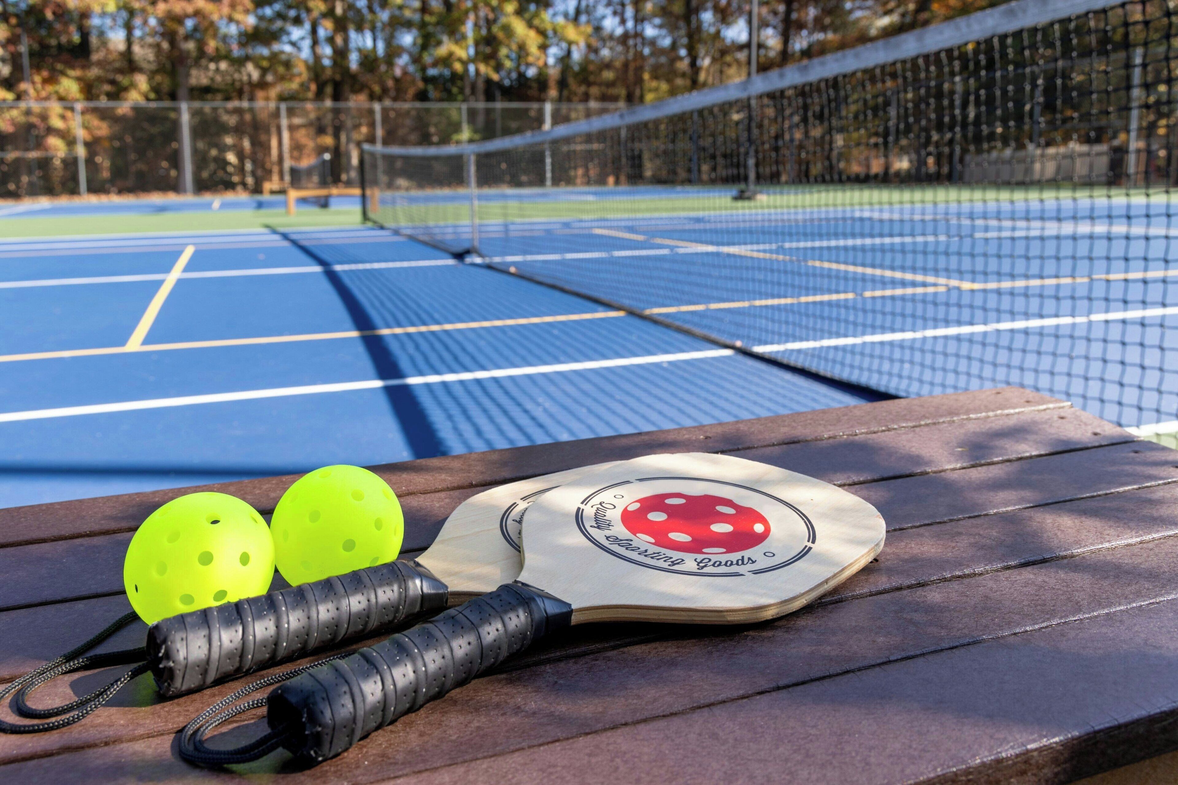 Un campo da tennis con una rete, una racchetta e due palline da tennis gialle su una panchina di legno.