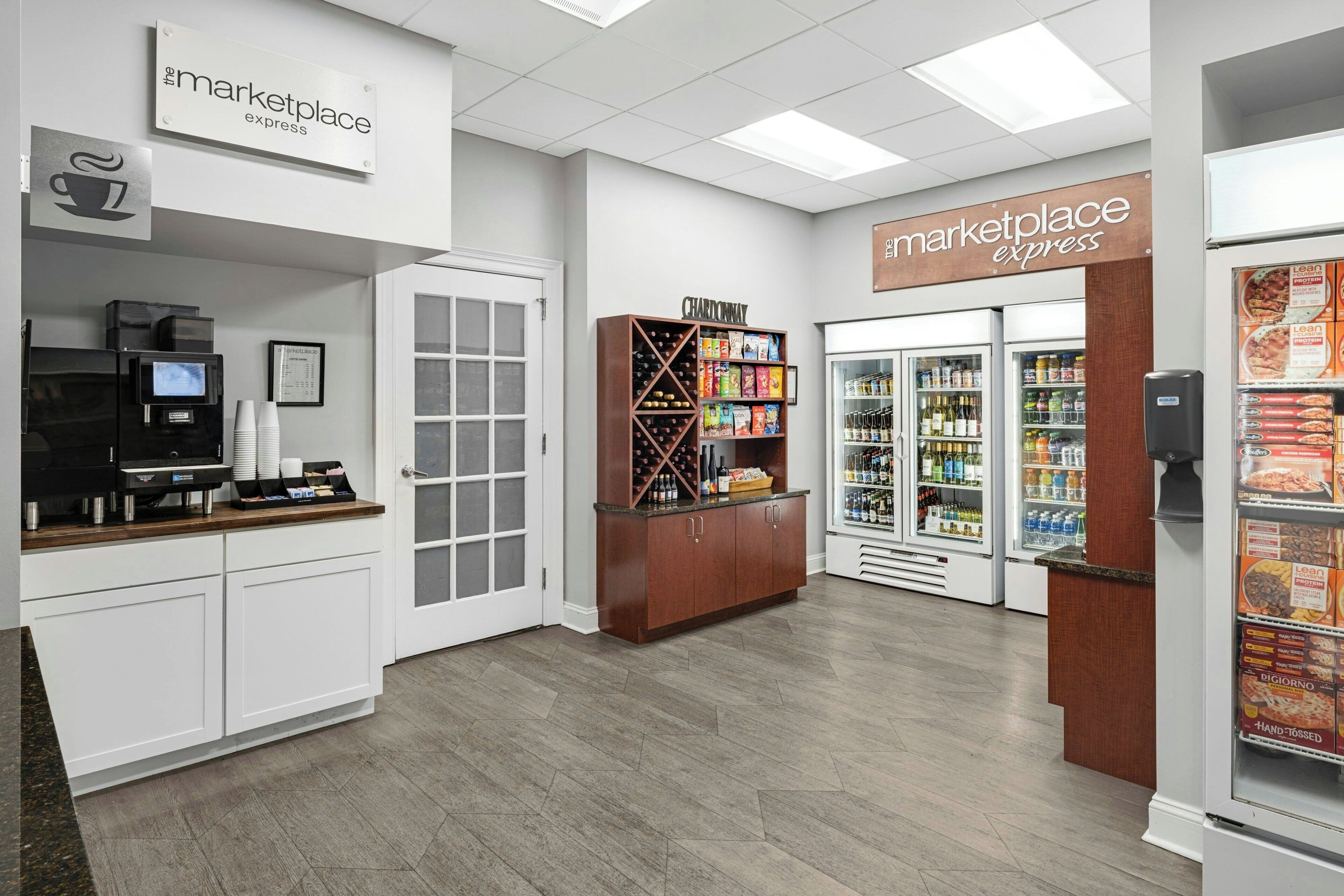 A clean, modern kitchenette area with a coffee machine, a wine cooler, and a refrigerated display case.