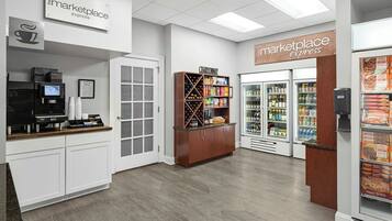 A clean, modern kitchenette area with a coffee machine, a wine cooler, and a refrigerated display case.