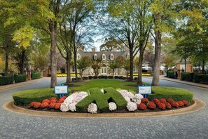 A landscaped garden with a symmetrical hedge design, a paved driveway, and a building with multiple windows in the background. - Marriott's Manor Club at Ford's Colony (Williamsburg)