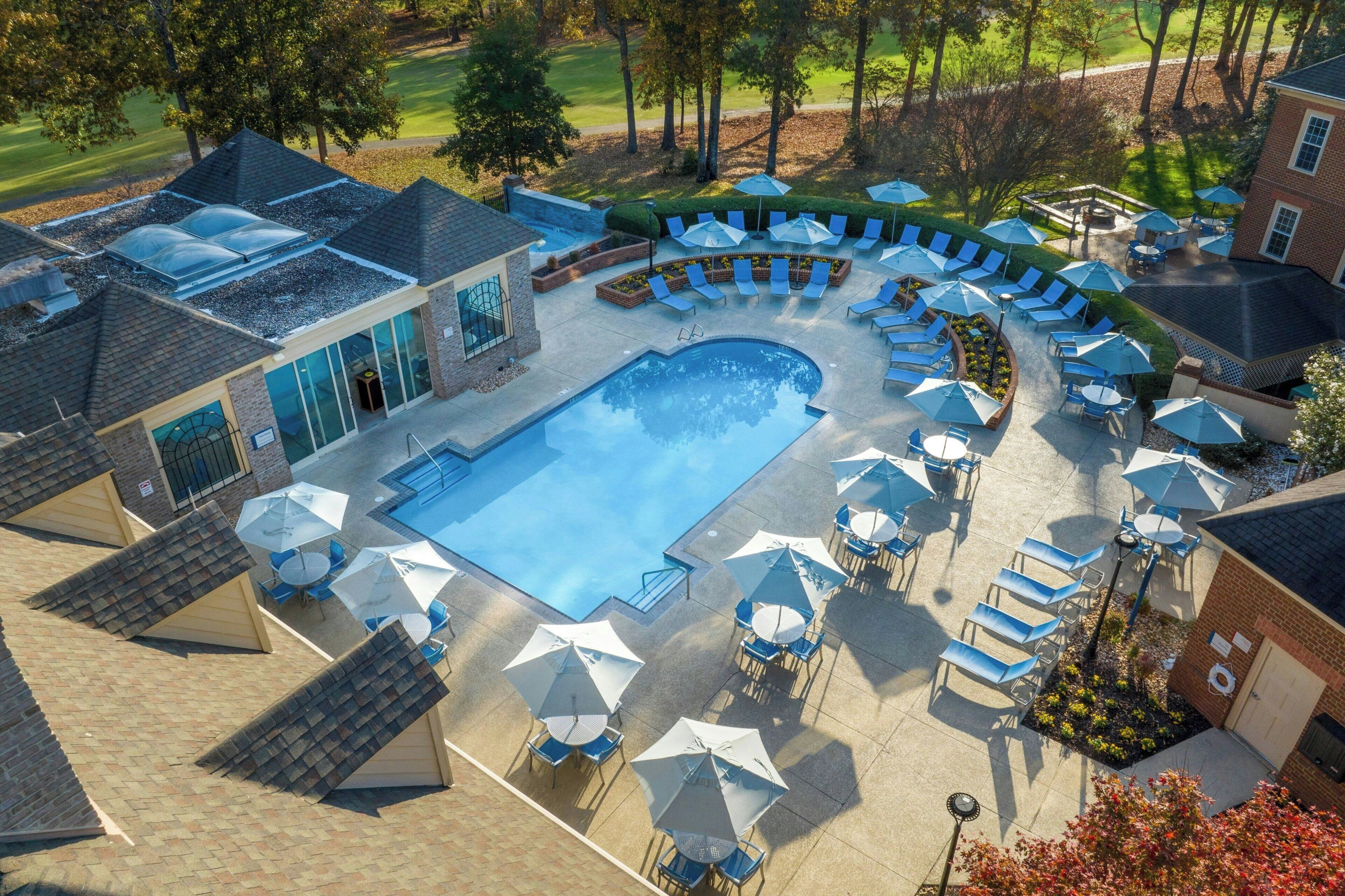 An aerial view of a resort with a swimming pool, lounge chairs, and umbrellas.