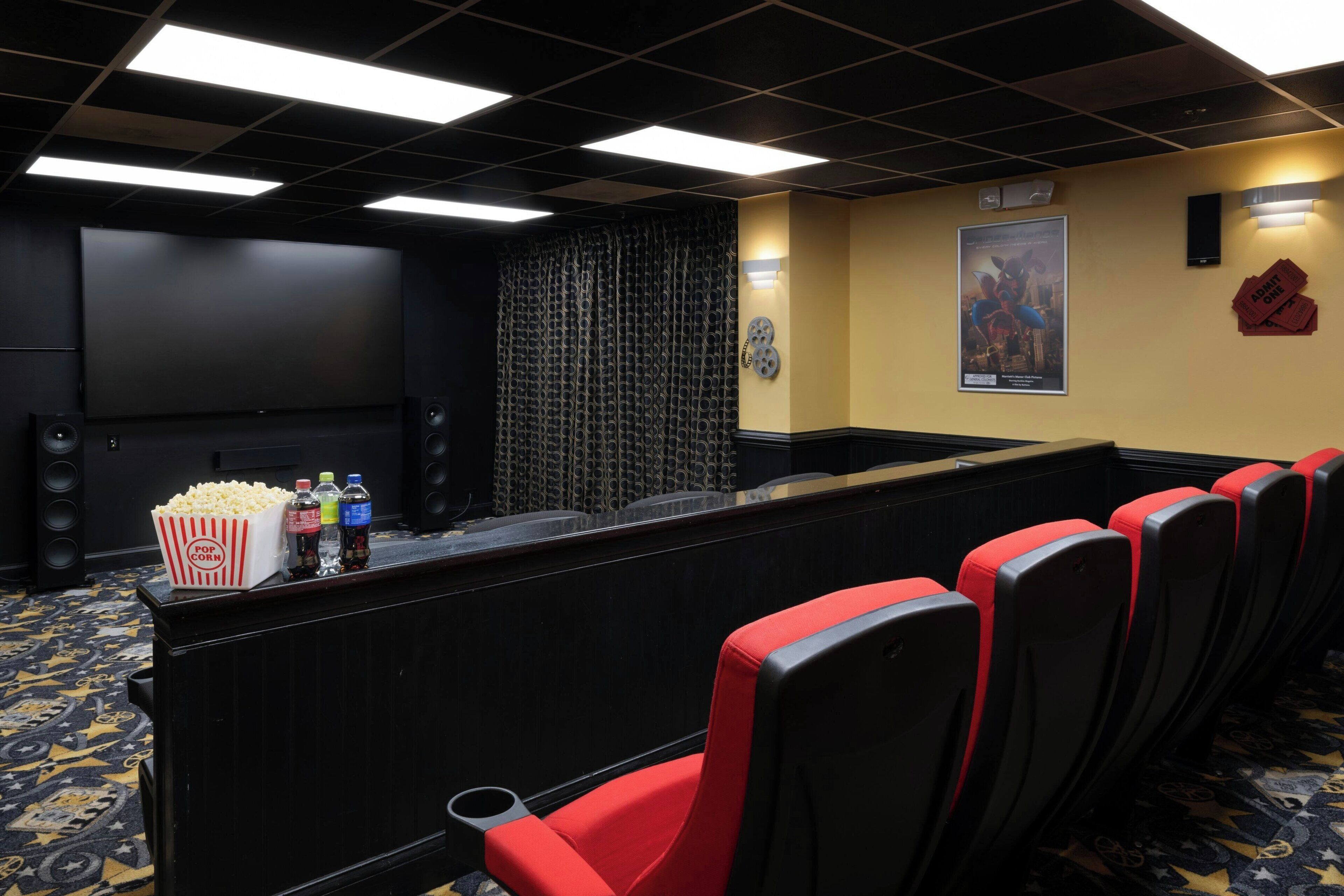 A theater with rows of red and black seats, a popcorn machine, and a large screen.