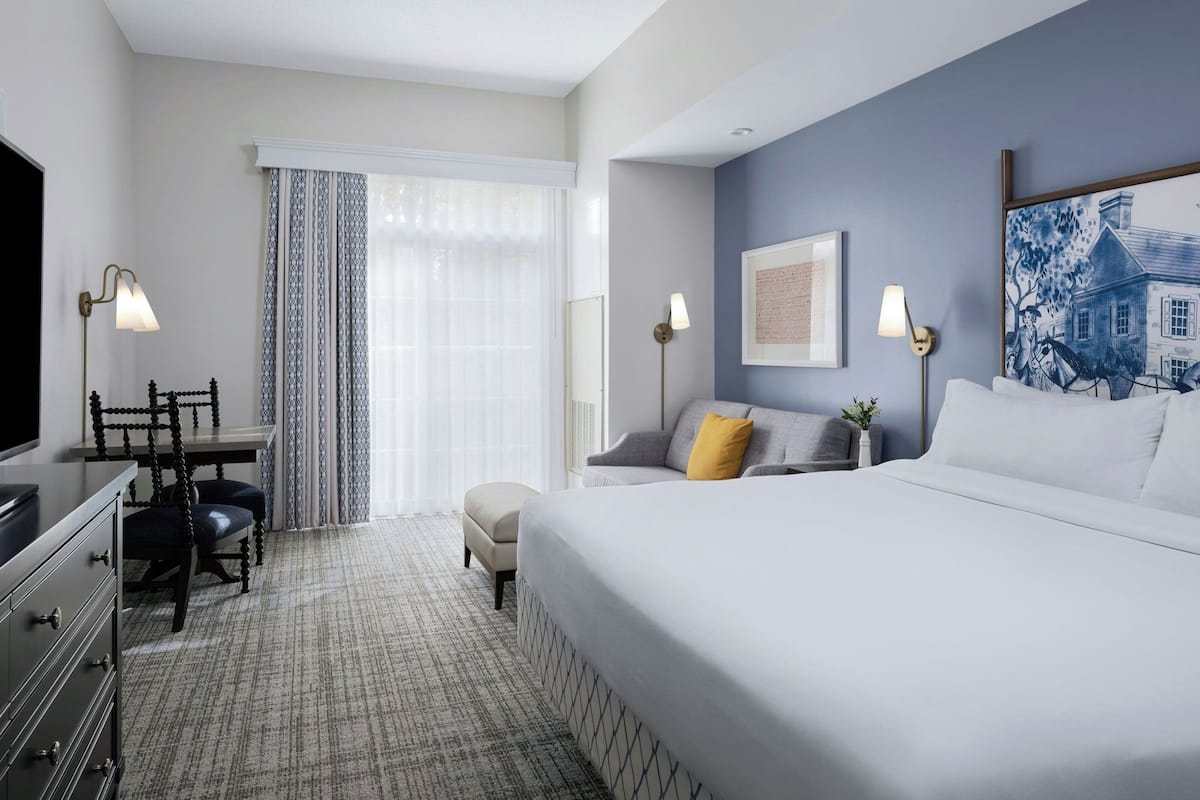A hotel room with a large bed, a desk with two chairs, a television, and a window with curtains.