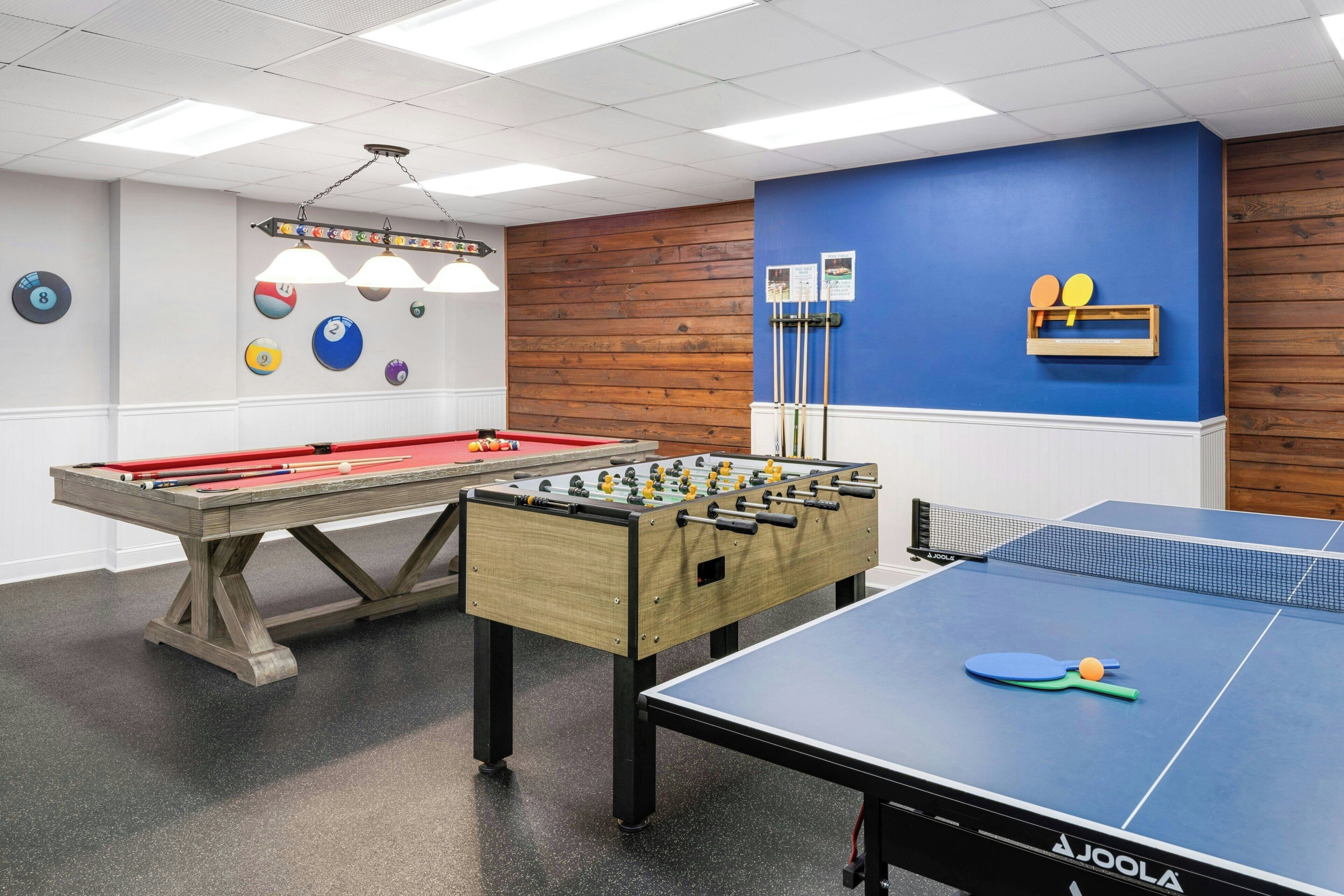 A recreational area with a pool table, foosball table, and ping pong table.