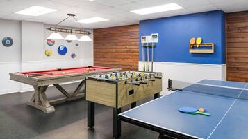 Un espacio recreativo con mesa de billar, mesa de futbolín y mesa de ping pong.
