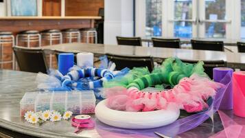 Un tavolo con materiali per creatività, tra cui tulle, nastri e perline, in una stanza con sedie e una finestra.