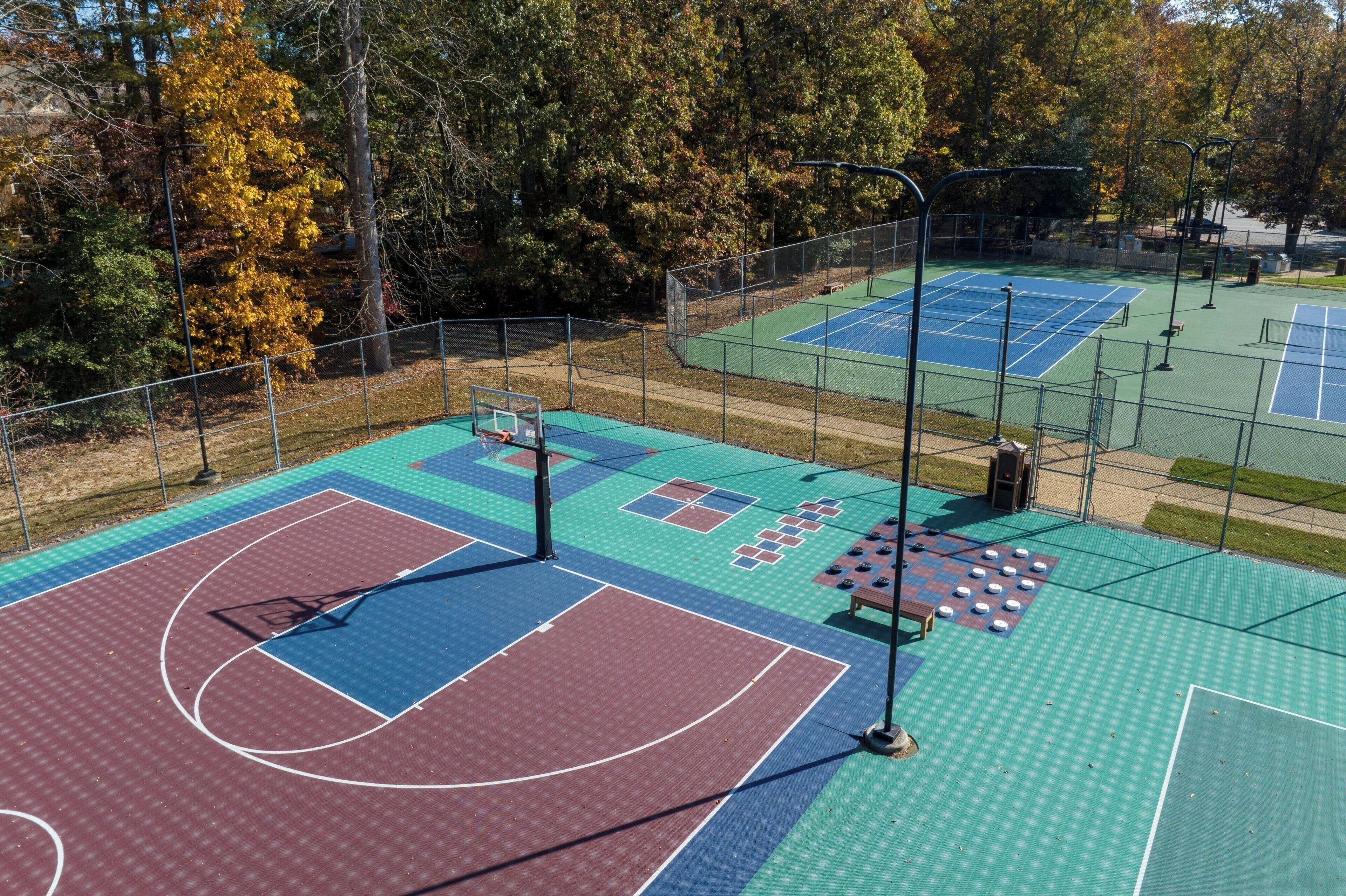 Een buitenbasketballbaan met meerdere velden, omringd door bomen en een hek.