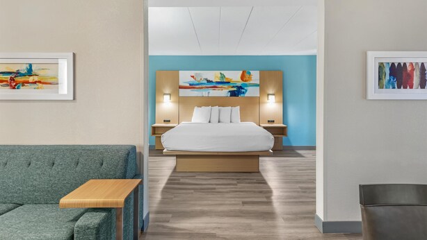 A modern hotel room with a large bed, a sofa, a wooden side table, and artwork on the walls. - Best Western PLUS Executive Hotel (Richmond)