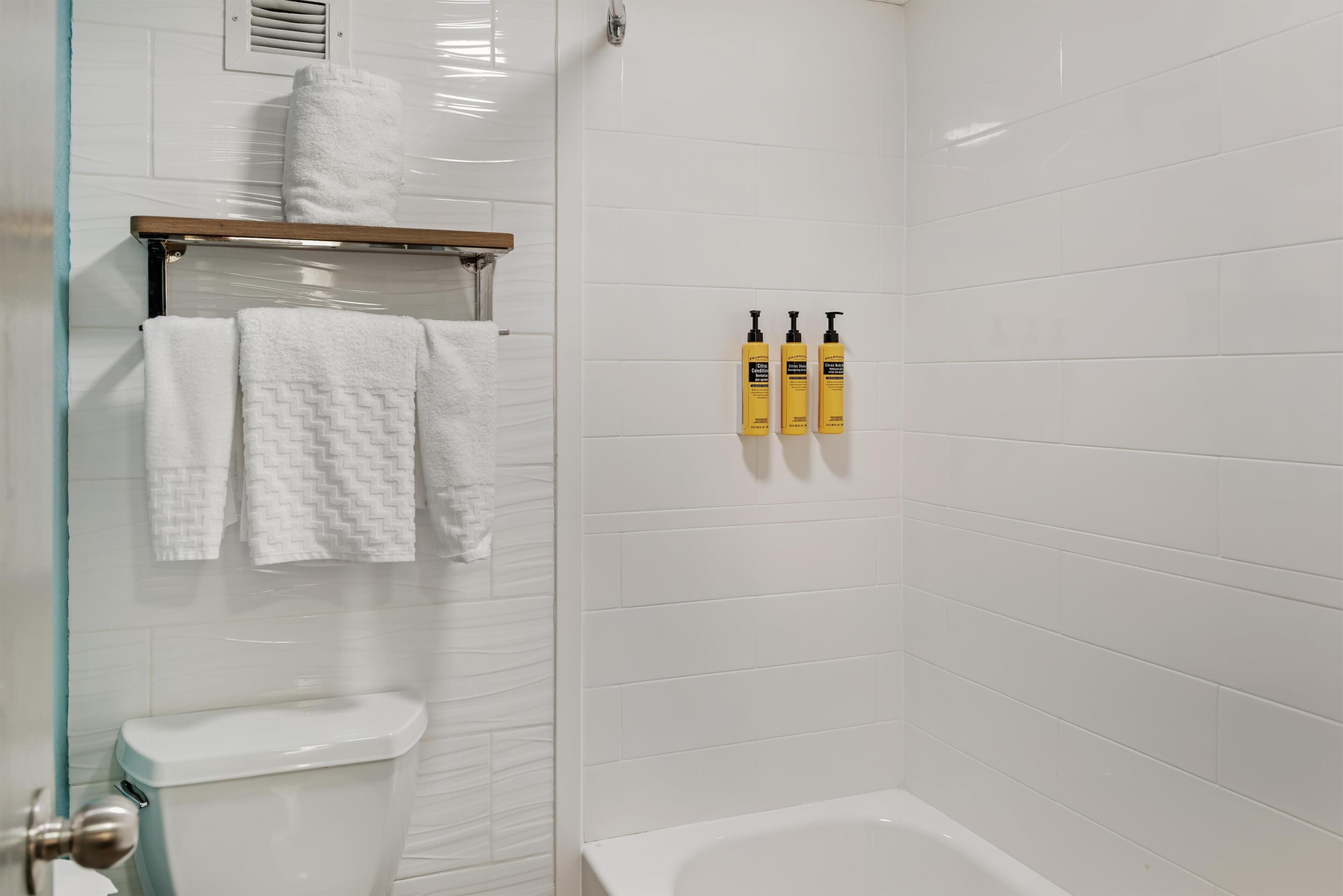 Une salle de bain avec des murs carrelés de blanc, une baignoire blanche, des toilettes et un porte-serviettes avec des serviettes blanches.