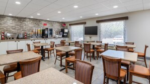 A restaurant with multiple tables and chairs, a kitchen area, and a television screen. - Best Western PLUS Executive Hotel (Richmond)