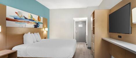 A modern hotel room with a bed, a TV, a painting, and a wooden desk.