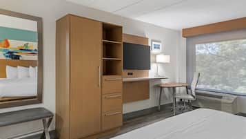 Habitación de hotel con una cama, un armario de madera, un escritorio con una silla, un televisor y un ventanal con vista a árboles.