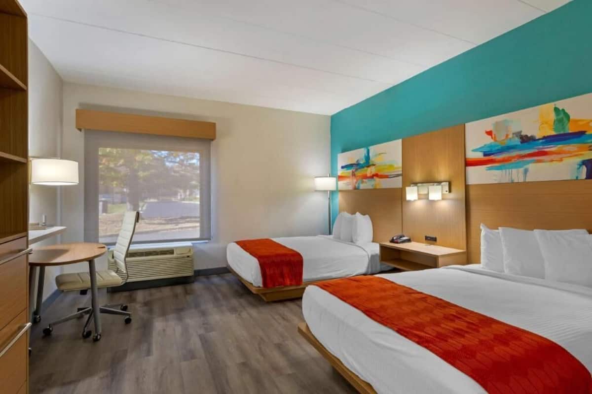 A hotel room with two beds, a desk, a chair, and a window with a view.