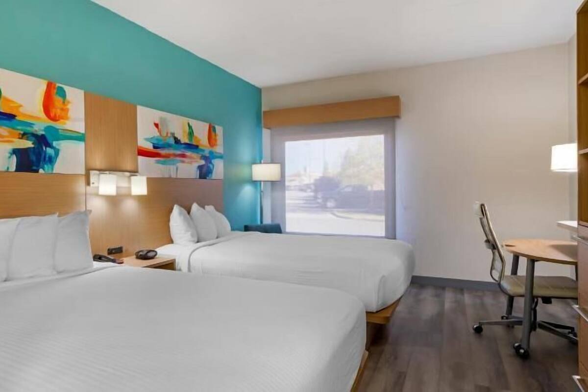 A hotel room with two beds, a desk, a chair, and a window with a view.