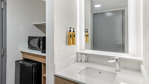 A modern bathroom with a white sink, a mirror, a microwave, and toiletries on the wall. - Best Western PLUS Executive Hotel (Richmond)