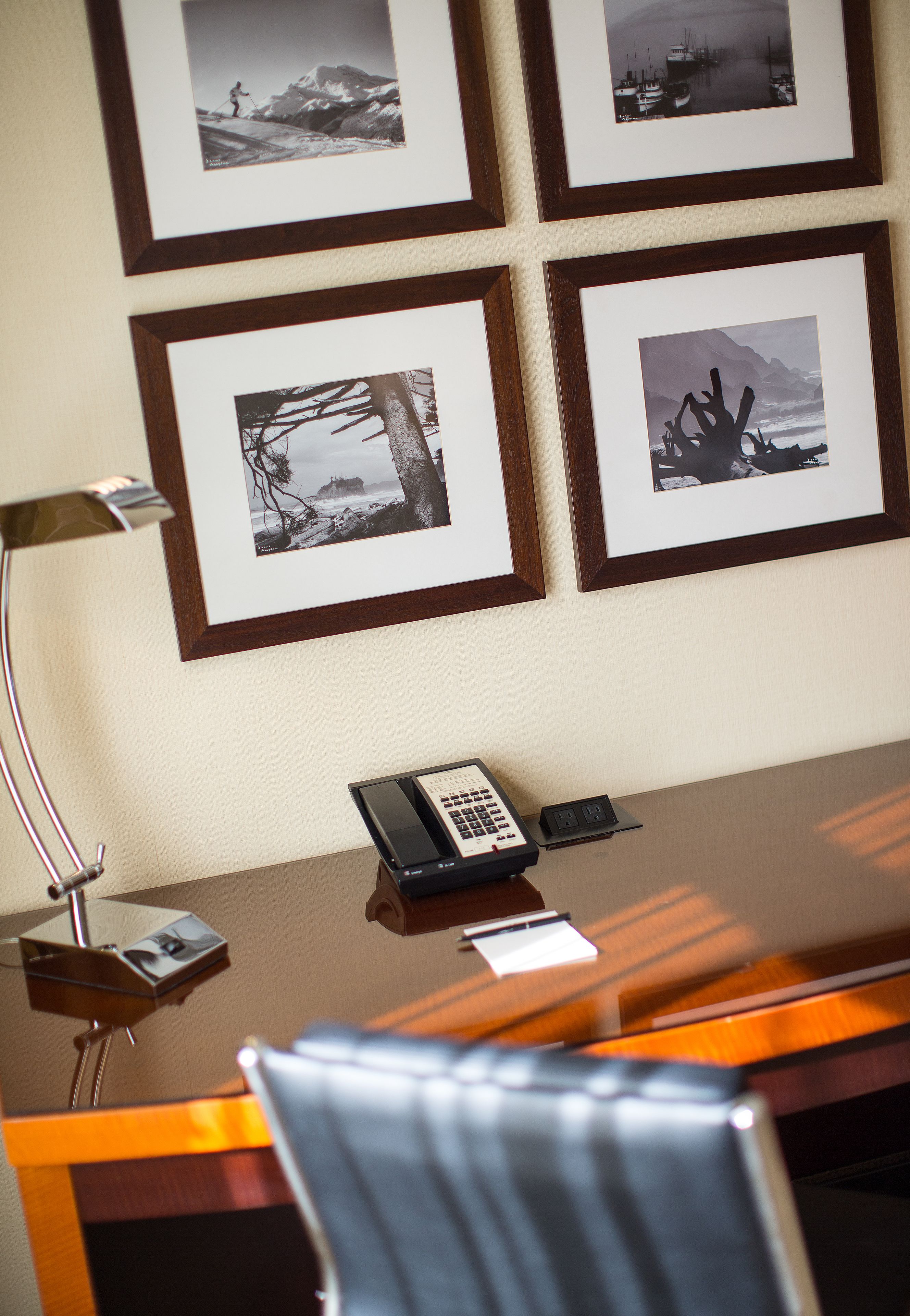 Une chambre d’hôtel avec un bureau en bois, un téléphone et des photographies encadrées accrochées au mur.